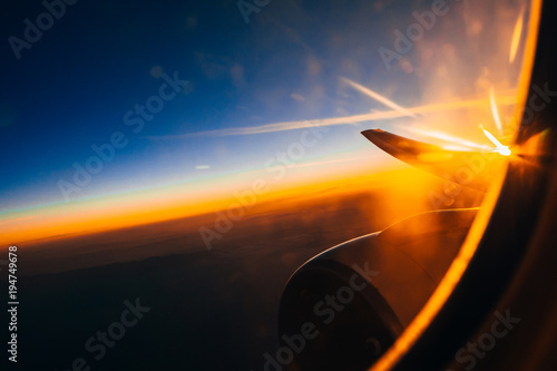 view through the window of the airplane on the wing and turbine at sunrise against the cloudy sky