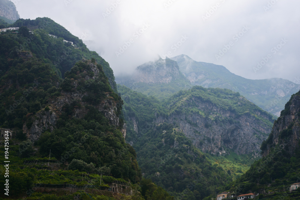 Green mountains in the clouds with rain and fog and blue rock at background. Touristic picture of jungle and rainforest, taken in Amalfi coast, in Italy