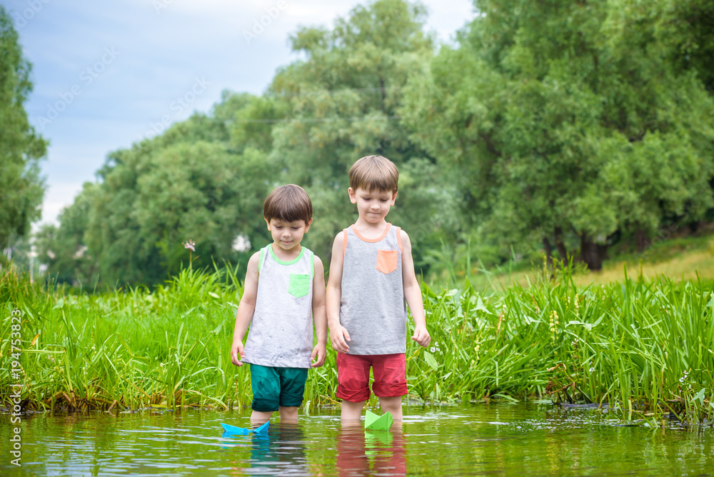 Two little brothers playing with paper boats by a river on warm and sunny summer day. Two little brothers playing with paper boats by a river on warm and sunny summer day.