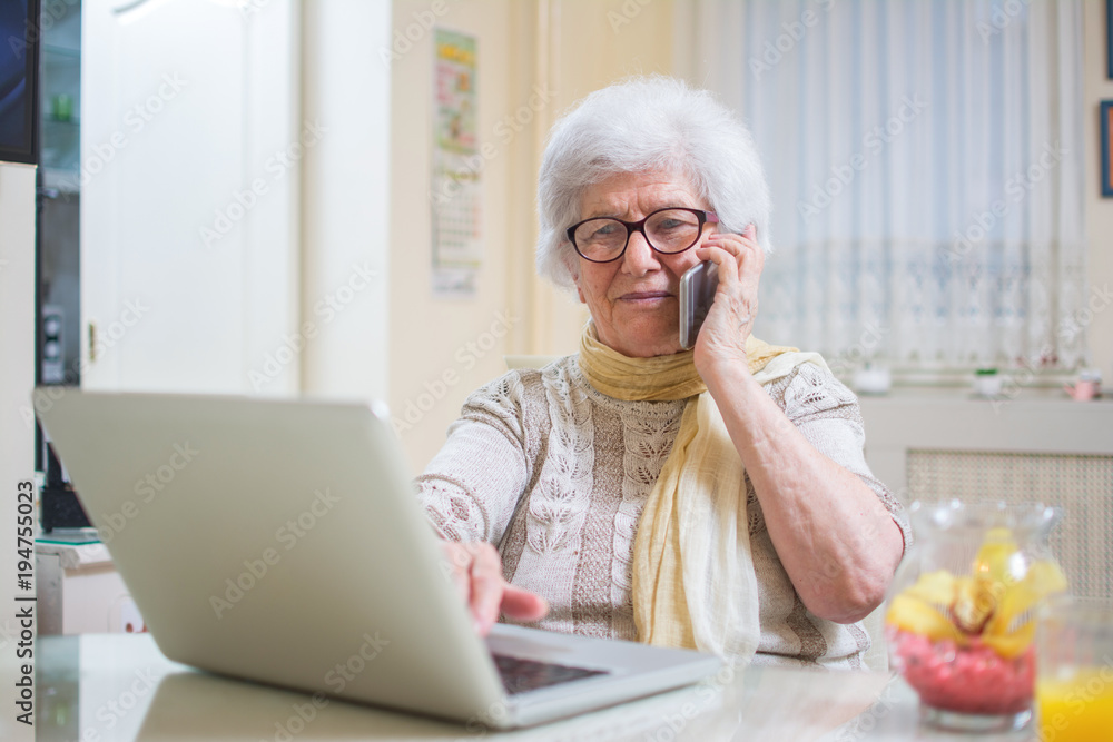 Smiling senior woman using phone and laptop at home. Smiling senior woman using phone and laptop at home.