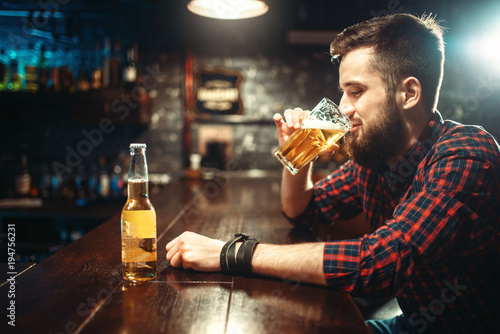 One bearded man drinks beer at the bar counter