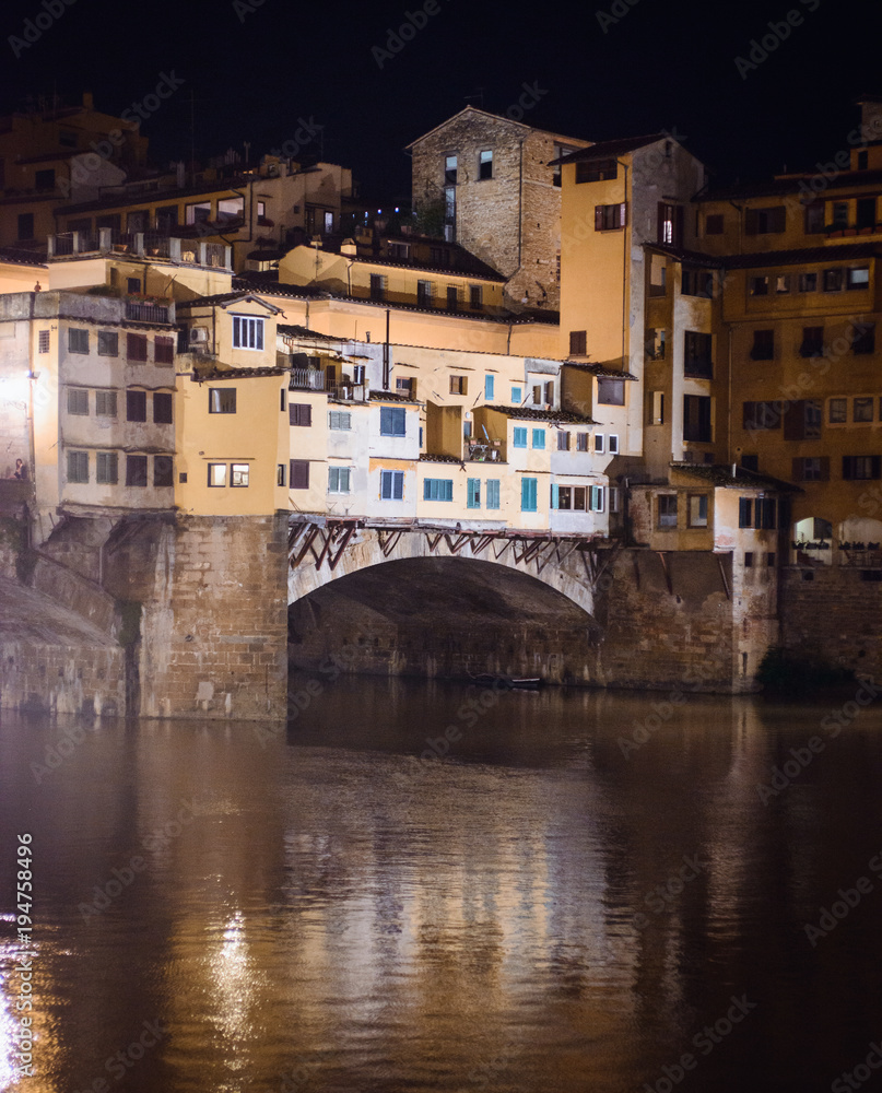 Night view of medieval stone bridge Ponte Vecchio and the Arno River from the Ponte Santa Trinita (Holy Trinity Bridge) in Florence Tuscany, Italy. Florence is a popular tourist destination of Europe