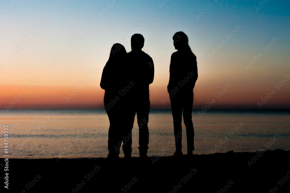 Silhouette of three friends in the morning at the beach looking at sunrise .