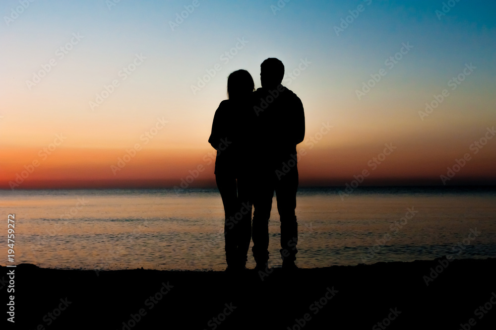 Silhouette of couple facing each other on the beach at sunrise.