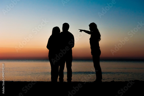 Silhouette of three friends in the morning at the beach looking at sunrise .