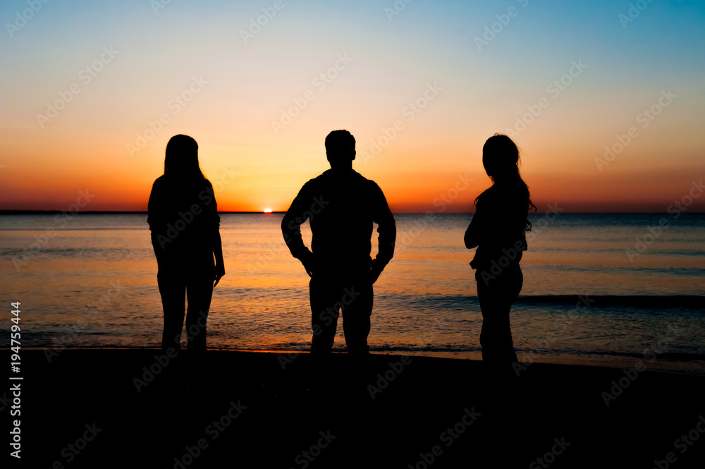Φωτογραφία Silhouette of three friends in the morning at the beach looking at sunrise
