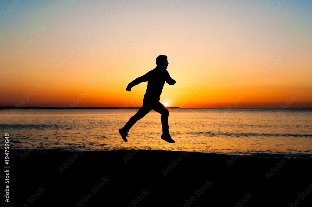 Silhouette of man jumping in the air on the beach at sunrise.