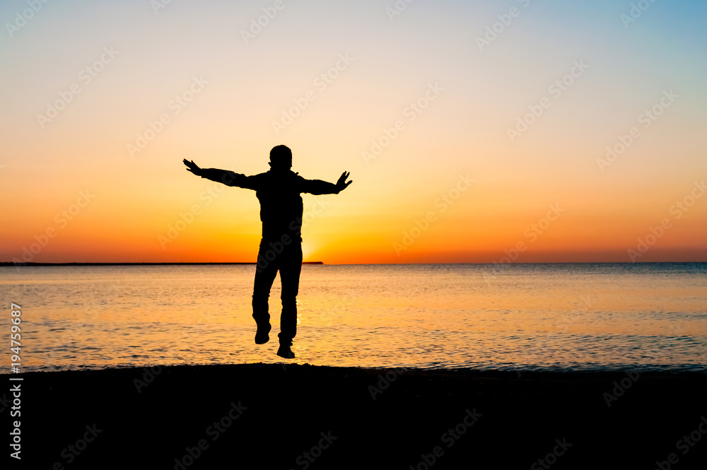 Silhouette of man jumping in the air on the beach at sunrise.