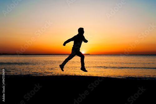Silhouette of man jumping in the air on the beach at sunrise.