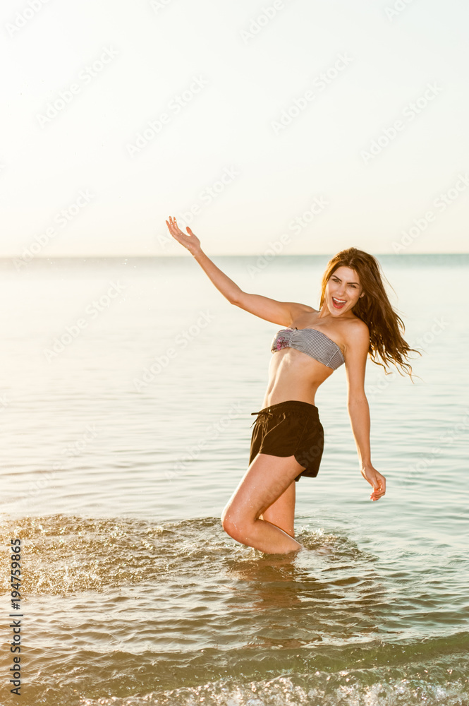 Naklejka premium Beach summer fun young woman splashing water, laughing, playing during summer holidays vacation on tropical beach.