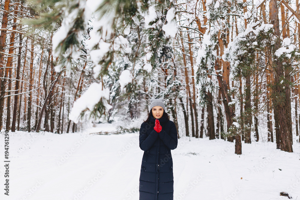 The girl walks in a snow-covered forest among the pines in red gloves