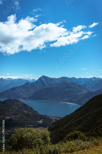 Panoramic View of beautiful landscape in the Italian Alps with fresh green meadows and snow-capped mountain tops in the background on a sunny day with blue sky and clouds in springtime