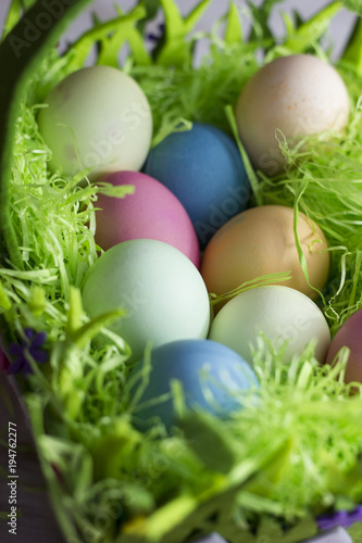 Colorful easter eggs in the decorative basket on a white wooden background