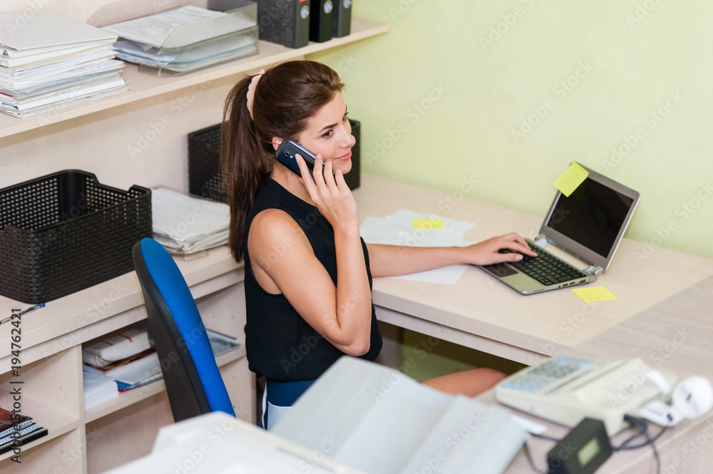 Young businesswoman sitting at desk in office, talking on cell phone, smiling. Young businesswoman sitting at desk in office, talking on cell phone, smiling.
