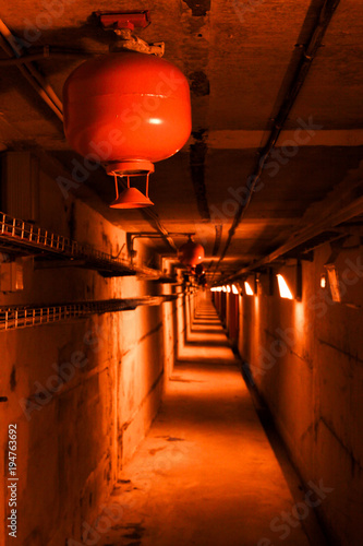 Psychedelic red deep in underground tunnel. Colored industrial background. Emergency lighting, row of fire extinguishers and cable telecommunication rack.