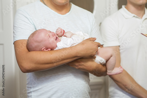 Godfather (caucasian young man) holding little infant kid in baptism (christening) ceremony in church