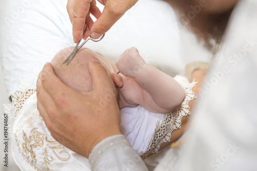 Abbe cutting hair to a little infant kid in baptism (christening) ceremony in church. Little scissors in his hand photo