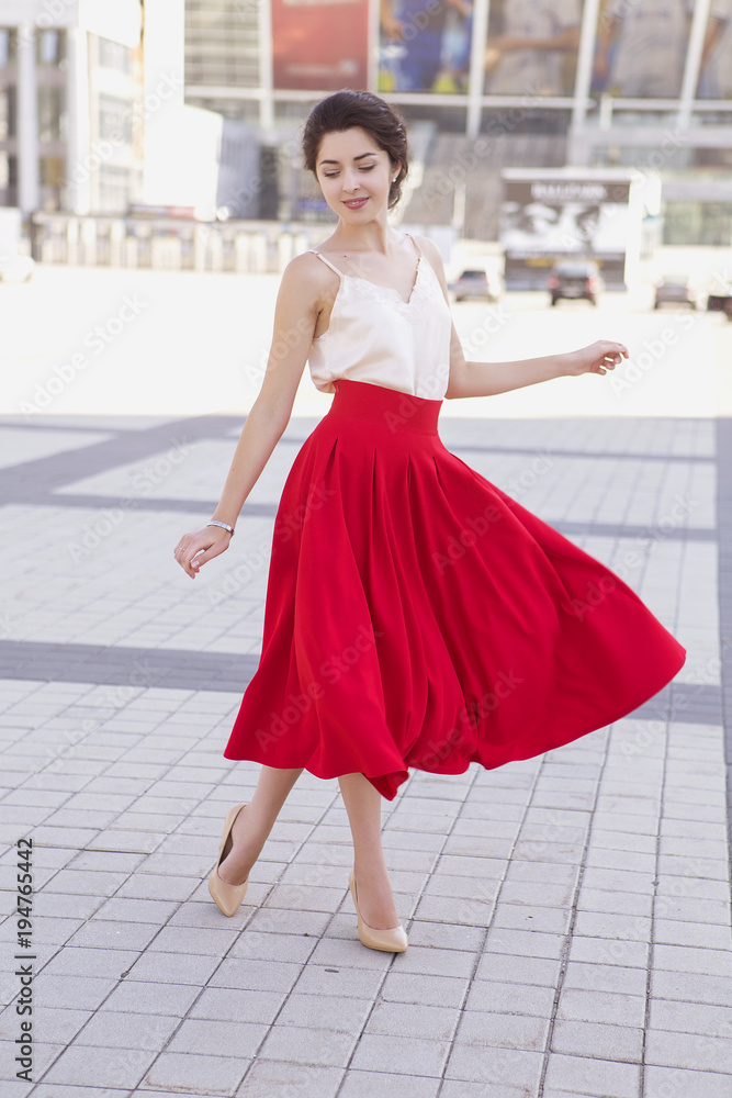 Young brunette caucasian woman in european city walking and relaxing. Summer sunny weather. She in red skirt and romantic blouse, smile happily. Copy space