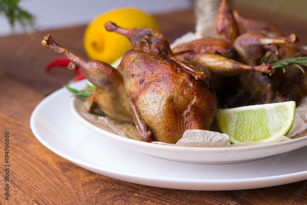 Appetizing baked quail with spices, herbs and lemon, lime in white dish on a wooden table Appetizing baked quail with spices, herbs and lemon, lime in white dish on a wooden table