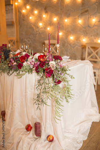 Set of wine color candles on a wedding table surrounded by light garland and flowers. Interior. Copy space