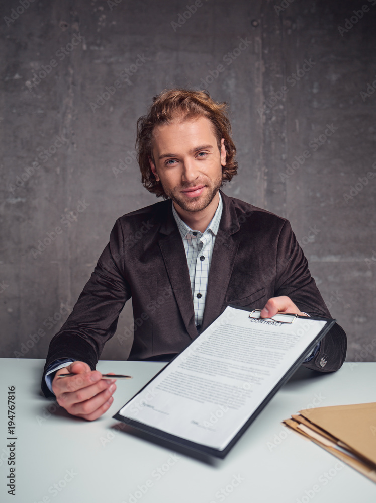 Portrait of positive unshaven man giving document for signing it. He locating at desk. Establishment of treaty concept Portrait of positive unshaven man giving document for signing it. He locating at desk. Establishment of treaty concept