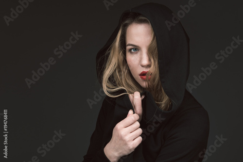 Photos Pretty anxious lady hiding under black hood and looking at camera with suspicion