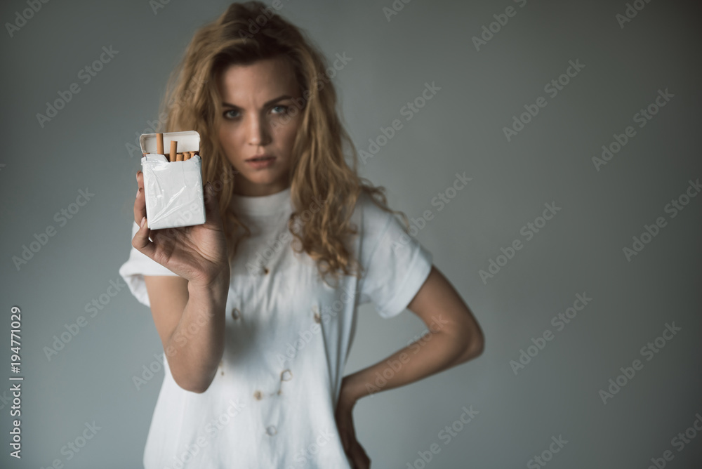 Waist up portrait of upset woman showing package with tobacco. Focus on smoke. Copy space in right side. Isolated on background Waist up portrait of upset woman showing package with tobacco. Focus on smoke. Copy space in right side. Isolated on background