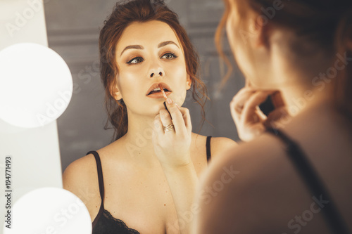 Brunette woman applying make up  paint her lips  for a evening date in front of a mirror. Focus on her reflection