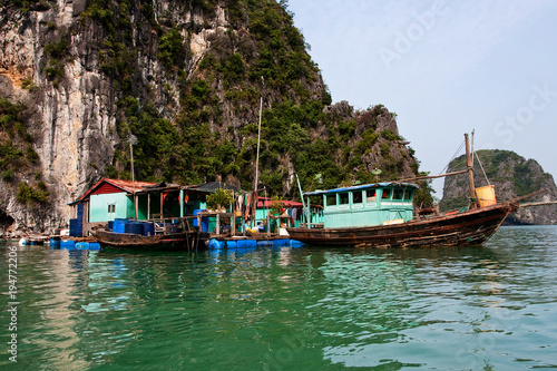 Floating village of Kuah Wan near the island of Daw Guo in Halong bay in Vietnam. National authentic ships with sails are floating by the sea. Houses on the water. Rocky coast. © Liliya Belaya