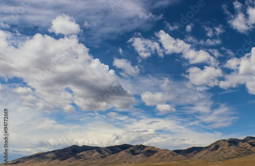 Rugged dessert hills in the distance under a huge fantastically blue sky with beautiful fluffy white clouds