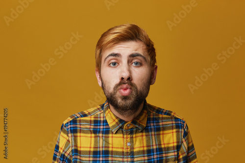 Portrait of fashionable male keeps lips round, wears plaid yellow shirt, isolated over yellow background. Surprise expression. © timtimphoto