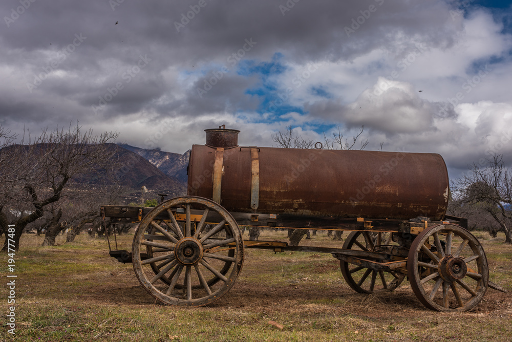 Vintage water tank trailer sitting under winter cloudy sky in the orchard.