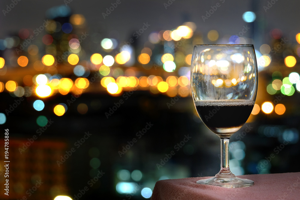 Red Wine Glass Placed on a table overlooking the hotel's backlight. Colorful city lights bokeh background.