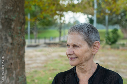 Portrait of beautiful older woman with short grey hair and black shirt in park (selective focus)