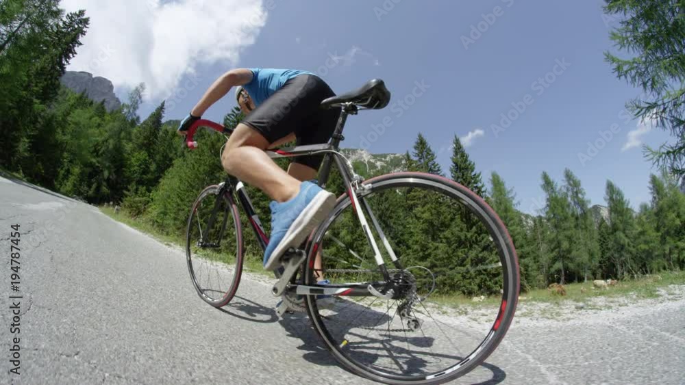 SLOW MOTION CLOSE UP: Unrecognizable young male cyclist riding his bike up an asphalt road on a beautiful day with a blue sky. Determined muscular biker vigorously trying to reach top of the hill. SLOW MOTION CLOSE UP: Unrecognizable young male cyclist riding his bike up an asphalt road on a beautiful day with a blue sky. Determined muscular biker vigorously trying to reach top of the hill.