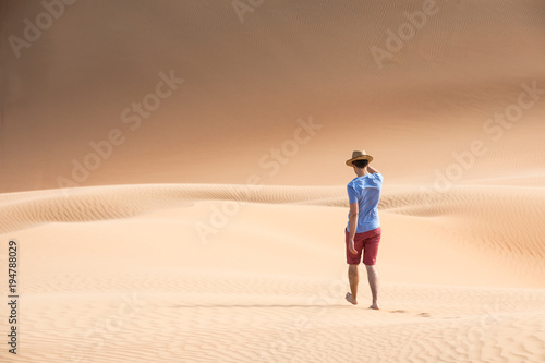 Young causasian male tourist in shorts hiking in giant Liwa desert dunes. Abu Dhabi, UAE. © Kertu