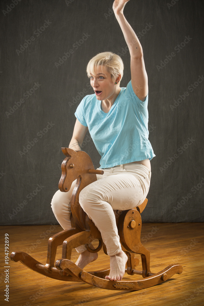 Young blonde woman riding wooden rocking horse in the studio. Stock Photo |  Adobe Stock