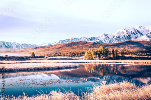 Mirror surface of the lake in the mountain valley. The peaks of the cliffs on the horizon at the colorful sky. Autumn weather