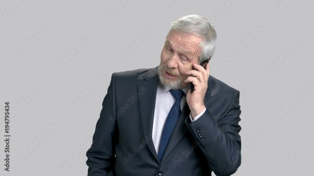 Elderly businessman talking on phone. Cheerful senior boss talking on mobile phone on grey background, portrait. Elderly businessman talking on phone. Cheerful senior boss talking on mobile phone on grey background, portrait.
