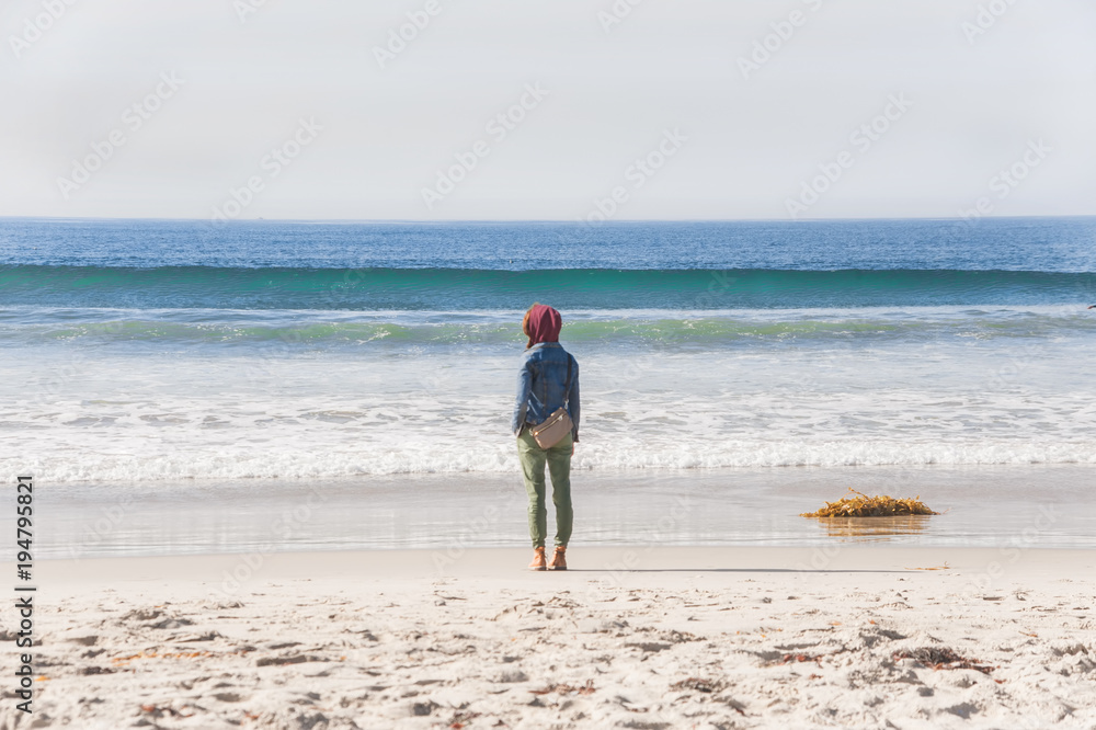 Frau steht alleine am Strand und schaut aufs Meer
