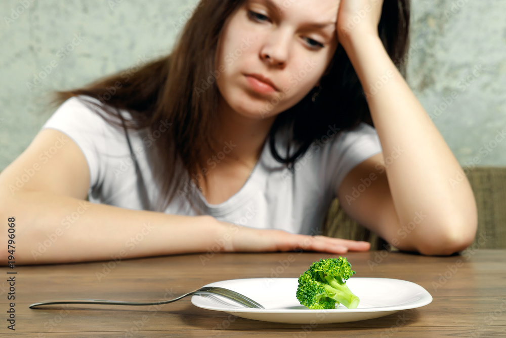 sad young brunette woman dealing with anorexia nervosa or bulimia having small green vegetable on plate. Dieting problems, eating disorder. sad young brunette woman dealing with anorexia nervosa or bulimia having small green vegetable on plate. Dieting problems, eating disorder.