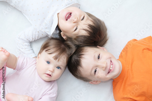 happy kids, three laughing children different ages lying, portrait of boy, little girl and baby girl, happiness in childhood of siblings, living in big family with three children