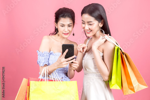 Portrait of two beautiful women holding shopping bags and enjoying shopping on pink background