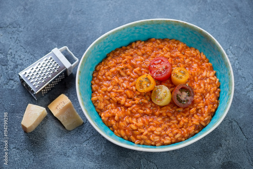 Plate with tomato risotto and parmesan cheese on a blue stone background, studio shot