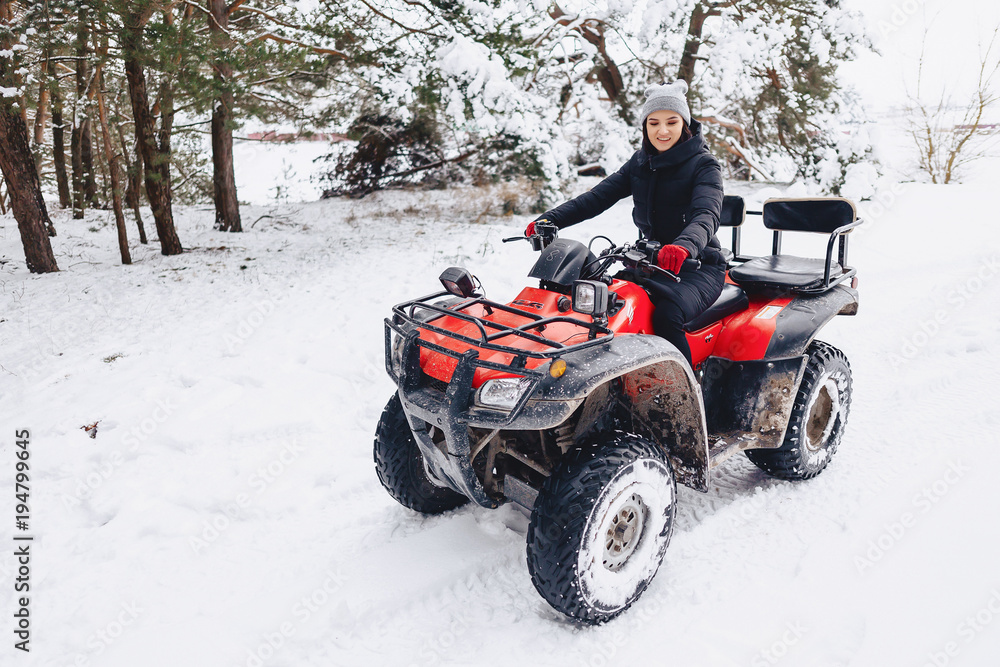 young girl on a motorcycle rides in snow-covered pine forest in winter