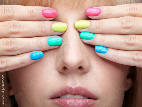 Young blonde woman with fun  varicoloured finger nails manicure.
