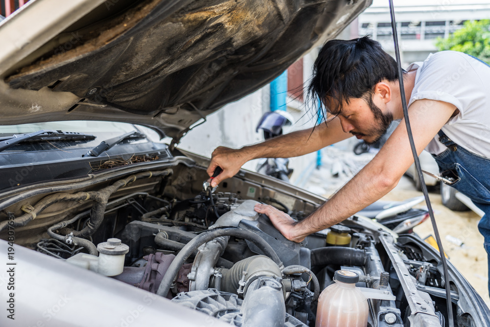 Fixing car engine in automobile repair garage. Handsome mechanics in uniform are repairing car while working in auto service Fixing car engine in automobile repair garage. Handsome mechanics in uniform are repairing car while working in auto service