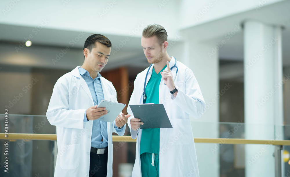 medical doctor professional team talked consult. Two young doctor Caucasian and Asian standing in hospital holding laptop and folder city building background. medical doctor professional team talked consult. Two young doctor Caucasian and Asian standing in hospital holding laptop and folder city building background.