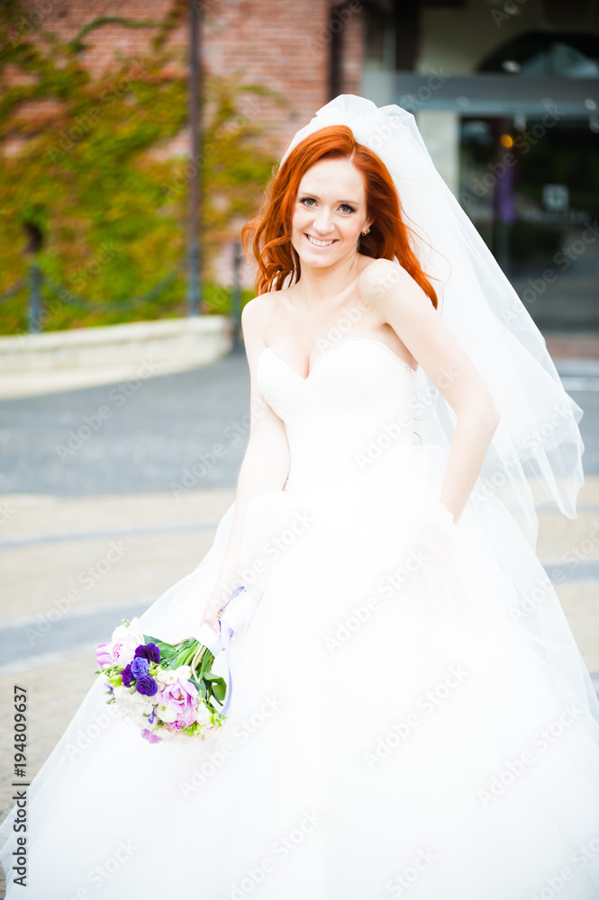 Beautiful red haired bride with wedding bouquet walking in the park near castle Beautiful red haired bride with wedding bouquet walking in the park near castle