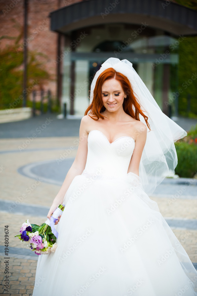 Beautiful red haired bride with wedding bouquet walking in the park near castle